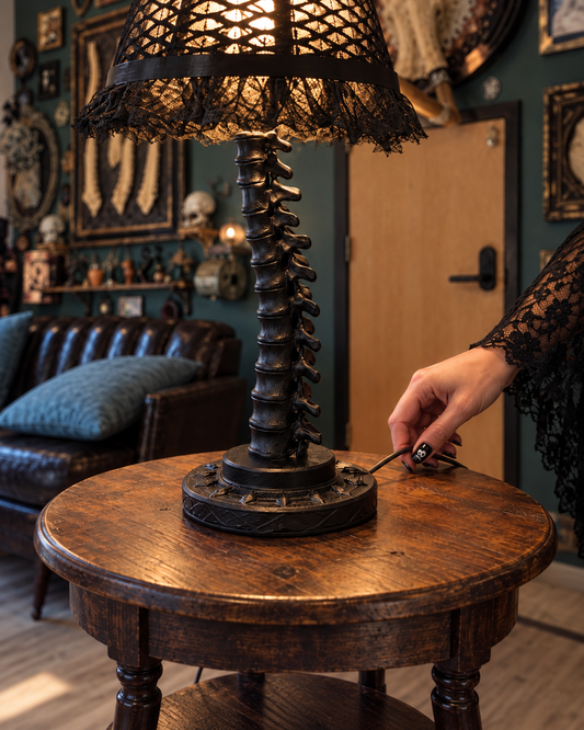 Close view of the black vertebral lamp stem, decorative base and cord beside Maya's hand