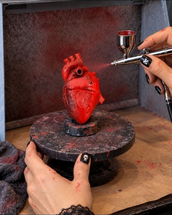 Hand-airbrushing a red anatomical heart in the Cozy AF Sweatshop