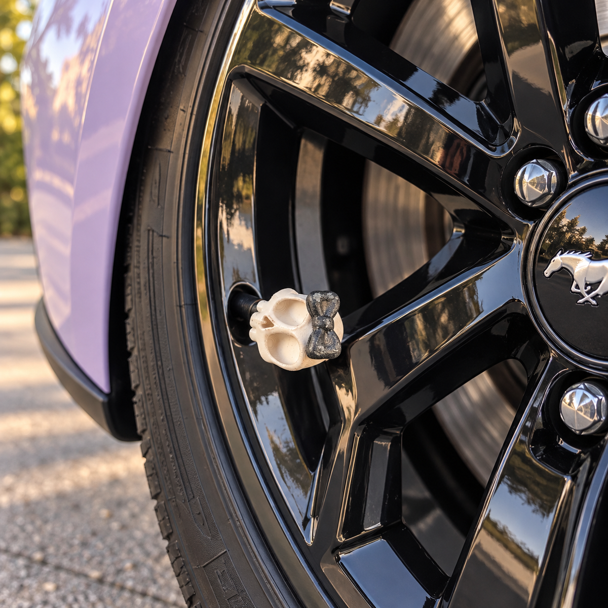 Styled scene of cream skull valve cap with a black bow on a clean black wheel beside lilac bodywork