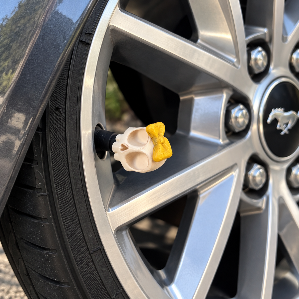 Styled color preview: cream skull valve cap with a yellow bow on a silver wheel beside charcoal bodywork