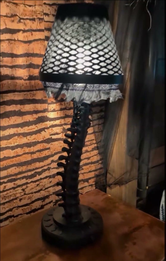 Real photo: The Librarian's Backbone matte black spine table lamp, lit, with fishnet and lace shade